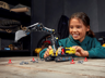 Enfant jouant avec la pelleteuse LEGO Technic 42121 assemblée, entourée de cônes rouges et de petites pièces grises