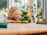 Enfant souriant jouant avec l'ensileuse LEGO Technic John Deere 9700 sur une table en bois dans un intérieur lumineux
