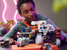 Jeune fille jouant avec le rover LEGO Technic 42180 sur une table, manipulant le bras articulé avant du véhicule