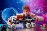 Garçon jouant avec le rover LEGO Technic 42180 sur fond cosmique bleu et violet, tenant le véhicule à deux mains