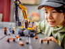 Gros plan d'un enfant souriant jouant avec la pelleteuse LEGO City 60420 et les minifigurines d'ouvriers sur un chantier miniature