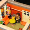 Intérieur détaillé du salon du club de musique avec minifigurine assise, table ronde jaune, canapé orange et disques vinyles au mur