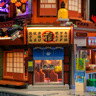 Gros plan sur l'entrée de l'izakaya avec enseigne lumineuse japonaise portant le kanji 酒 (saké) et rideau noren bleu