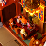 Vue plongeante sur la table de banquet miniature avec dinde rôtie, bougies et figurines attablées sous un lustre LED