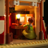 Détail intérieur éclairé du cirque Lumibricks montrant une figurine féminine en robe verte préparant de la nourriture dans les coulisses
