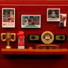 Mur de trophées du club de boxe avec coupe dorée, gant rouge, ceinture de champion et photos encadrées